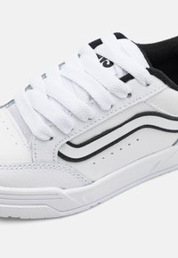 Baskets blanches avec un cuir texturé et des panneaux en maille. Présente des accents noirs, des lacets blancs plats et une semelle en caoutchouc avec un motif de semelle.
