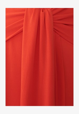 Punane kangas, millel on pehme ja tekstuurne viimistlus, omades volditud külgi ja sõlm detaili, luues voolava ja struktureeritud välimuse.