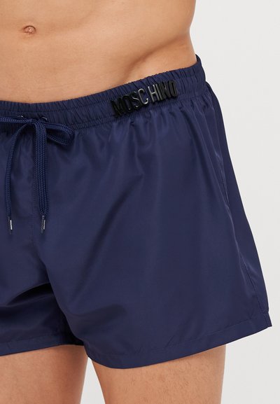 Tmavomodré plavky vyrobené z hladkej, ľahkej tkaniny, s elastickým pásom a šnúrkou na stiahnutie a čiernym logom "Moschino".