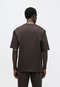 Brown short-sleeve t-shirt made of cotton, featuring a crew neck and a loose fit. Smooth texture with no visible patterns or accents.