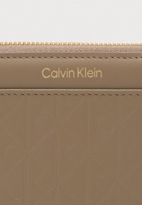 Calvin Klein világosbarna bőr pénztárca domború geometrikus mintával, arany logóval és cipzáras záródással. Simább textúra, részletes varrással.