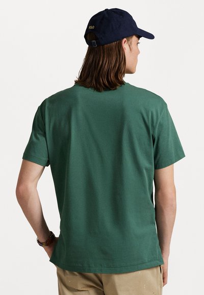 Groene katoenen t-shirt met een ronde halslijn en korte mouwen, van achteren getoond, gecombineerd met een marineblauwe honkbalpet met gouden borduursel.