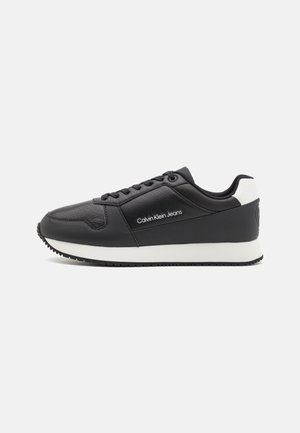 Black leather sneaker with a white heel and sole. Features a smooth texture and logo near the laces. Classic round toe design.