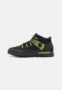 Scarpe da trekking mid-top in nero e verde. Parte superiore in mesh e materiale sintetico, distintivo accento verde, lacci rosa, suola testurizzata con motivi di grip.