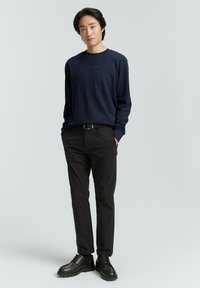 Navyblauwe langemouwen shirt met een subtiel logo op de borst, gecombineerd met zwarte slim-fit broek en zwarte veterschoenen.