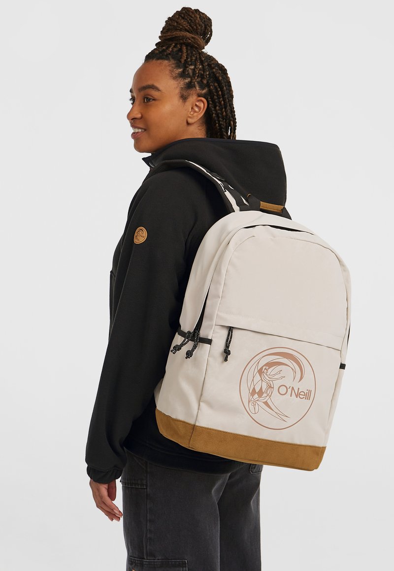 Beige rugzak met een bruine onderkant, zwarte accenten en een circulair O'Neill logo. Beschikt over twee zijzakken en verstelbare schouderbanden.