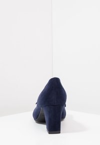 Scarpa con tacco alto in suede blu navy, con punta arrotondata e tacco affusolato, caratterizzata da una texture liscia e una silhouette semplice.