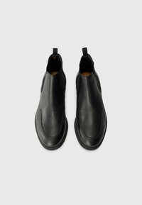 Bottes chelsea noires en cuir avec une texture lisse, des panneaux latéraux élastiques et des languettes pour un enfilage facile. Design à bout arrondi et semelle profilée basse.