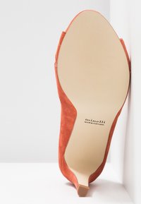 Chaussure à talon haut en daim couleur rouille, vue de la semelle, avec la marque "minelli" et le texte "Fabriqué au Portugal" visibles.