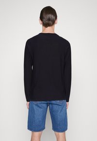 Schwarzes Langarmshirt aus weichem Stoff; von hinten betrachtet. Kombiniert mit blauen Denim-Shorts, die einen lässigen Schnitt und Design zeigen.