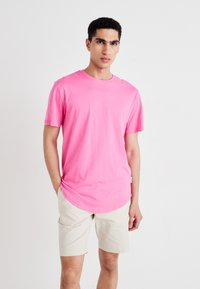 Rožinės spalvos medvilniniai marškinėliai trumpomis rankovėmis, suapvalintu kaklu ir išlenktu apvadu. Dėvimi su šviesiai rudos spalvos šortais, turintys laisvą prigludimą ir lygią tekstūrą.