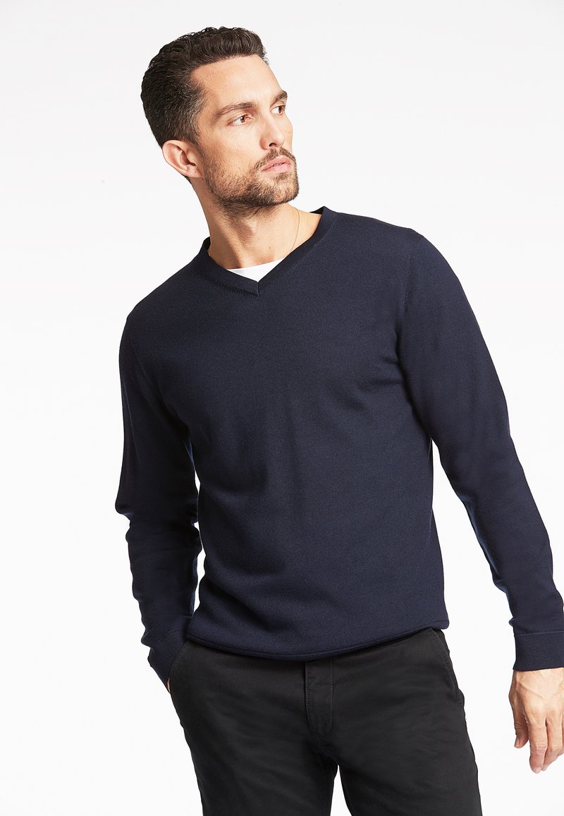 Maglione blu navy a scollo a V realizzato in tessuto morbido, con maniche lunghe e superficie textured, abbinato a pantaloni neri.