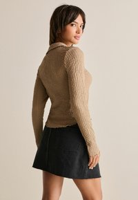 Långärmad, texturerad beige topp med krage, kombinerad med en svart denimminikjol med fransar i botten och bakfickor.