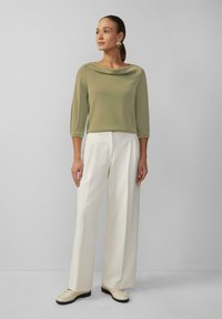 Haut vert olive clair avec un col drapé, manches trois-quarts, associé à un pantalon large blanc et des mocassins crème. Tissu texturé.
