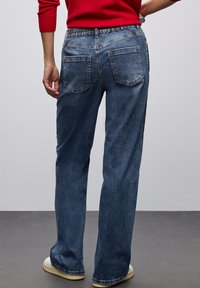 Jeans de denim con corte relajado, color azul oscuro, cinturilla elástica y dos bolsillos traseros. La tela tiene una textura ligeramente desgastada.