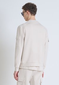 Beige sweatshirt met een ronde hals, lange mouwen en een zijzakdetails. Glad textuur en een ontspannen pasvorm, gecombineerd met bijpassende broeken.