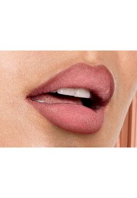 Rouge à lèvres nude mat appliqué sur des lèvres pulpeuses, mettant en valeur une texture lisse et un éclat subtil sur la peau environnante.