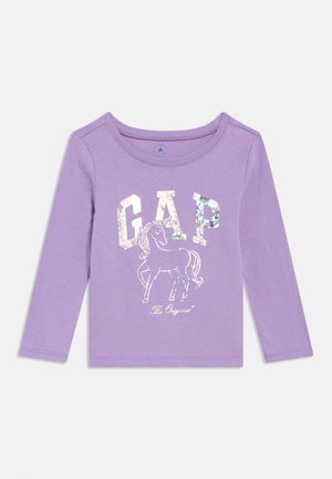Lilakkrāsas garām piedurknēm toddler krekls ar metāliskām burtiem "GAP" un hologrāfisku vienradža ilustrāciju krekla priekšpusē centrā.