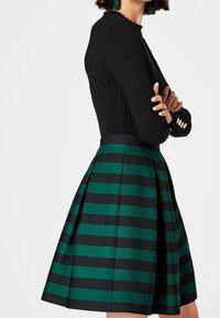 Suéter negro de canalé con mangas largas combinado con una falda plisada de rayas verdes y negras. La falda cuenta con un cinturón y una forma estructurada.