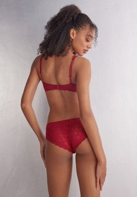 Rotes Spitzenunterwäsche-Set mit einem BH mit verstellbaren Trägern und gewellten Kanten, kombiniert mit passenden Spitzenpantys im gleichen Design.