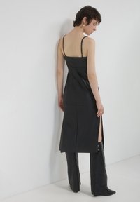 Schwarzes Lederkleid mit dünnen Trägern, tailliertem Oberteil und hohem Schlitz. Das Design bietet eine glatte Textur und eine schlanke Silhouette.