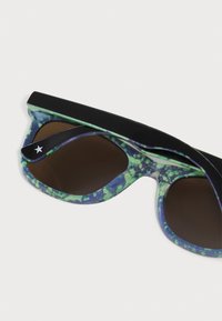Pārlielās saulesbrilles ar melnu un zaļu marmora rakstu rāmī ar spīdīgu apdari un tumši brūnām lēcām, papildinātas ar mazu zvaigžņu emblēmu.