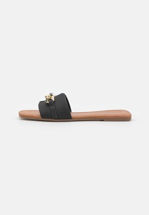 Flat slide sandal with black broad strap adorned with a gold chain detail and tan cushioned sole on white background.