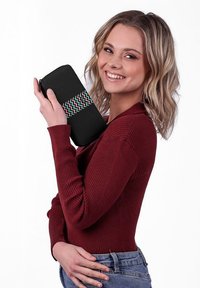 Black zippered wallet made of fabric with a colorful zigzag pattern. Model holds it against a plain background, wearing a burgundy top.