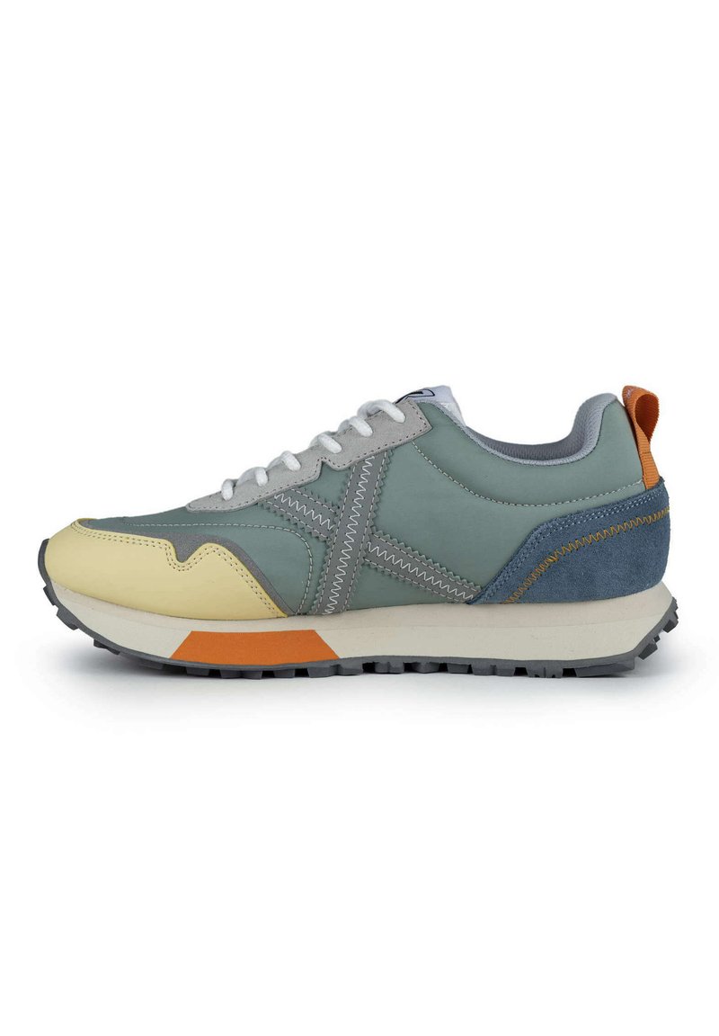 Zapatillas deportivas que combinan materiales en tonos gris, verde y amarillo, con acentos de ante texturizado, cordones blancos y una suela negra resistente.