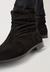 Černé semišové kotníkové boty s volně sklopeným designem, kontrastním prošíváním a nízkým gumovým podpatkem pro větší podporu.