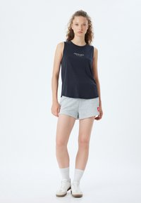 Navy mouwloze top met de print "CREATE YOUR FUTURE"; gecombineerd met lichtgrijze shorts; model draagt witte sneakers en geribbelde sokken.