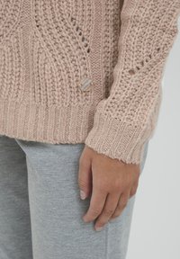 Maglione a maglia rosa chiaro con un motivo testurizzato e un orlo a costine, decorato con un bottone tondo e opaco vicino alla vita.