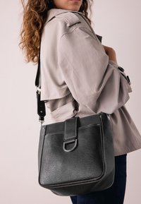 Black leather handbag with silver stitching and hardware, featuring a front flap and adjustable strap. Worn on the shoulder.