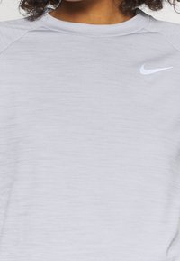 Vaalea harmaa urheilupaita, jossa on sileä pinta, pyöreä kaula-aukko ja valkoinen Nike-logo vasemmalla puolella. Sisältää raglan-hihat liikkuvuutta varten.