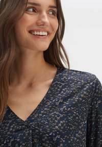 Marinebluse mit V-Ausschnitt-Design, ausgestattet mit einem strukturierten Leopardenmuster in Beige- und Weißtönen. Weicher, fließender Stoff.