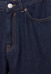 Close-up of dark blue denim jeans with orange stitching, metal button, coin pocket, and main front pocket visible.