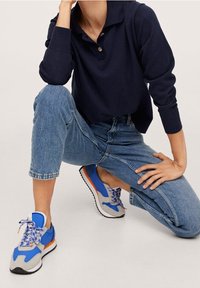 Niebieskie trampki z szarymi akcentami i pomarańczowymi detalami; zestawione z jasnoniebieskimi, skróconymi dżinsami oraz granatową koszulką polo z kołnierzykiem i guzikami.