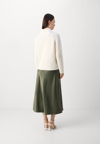 Kremfarget ribbestrikket genser med høy krage, kombinert med en shiny olivengrønn midikjole og beige høyhælte sandaler. Jevne teksturer og harmoniske farger.