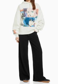 Vit hoodie med grafiska tryck av två animekaraktärer, med färgglada accenter. Parat med svarta vida byxor och sneakers.