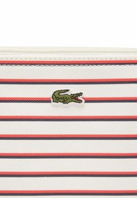 Pochette bianca a strisce con sottili linee rosse e blu navy. Presenta il logo ricamato di un coccodrillo verde. Tessuto texturizzato con una finitura elegante.