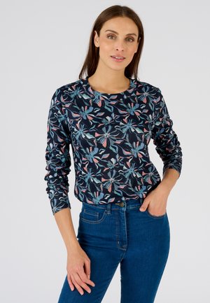Marineblauwe blouse met lange mouwen en een bloemenpatroon in lichtblauw en roze. Zachte katoenen stof, ronde halslijn, slim fit, gecombineerd met blauwe spijkerbroeken.