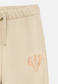 Calças de moletão bege com cintura elástica, cordão, bolso lateral e logótipo GAP desbotado com uma gráfica da Minnie Mouse na perna.