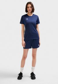 Mörkblå atletisk T-shirt och shortsset, tillverkat av lätt tyg, med rund halsringning och logodetaljer. Svarta sneakers och vita strumpor.