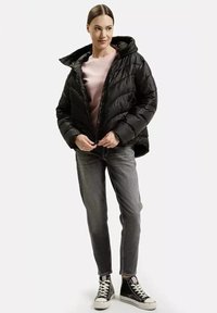 Czarna puchowa kurtka z kapturem, z pikowanym wzorem i zapięciem na zamek, noszona na jasnoróżowej bluzie i szarych dżinsach.