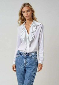 Blouse blanche à manches longues avec col à volants et devant à boutons, associée à un jeans taille haute bleu clair. Tissu lisse et coupe décontractée.