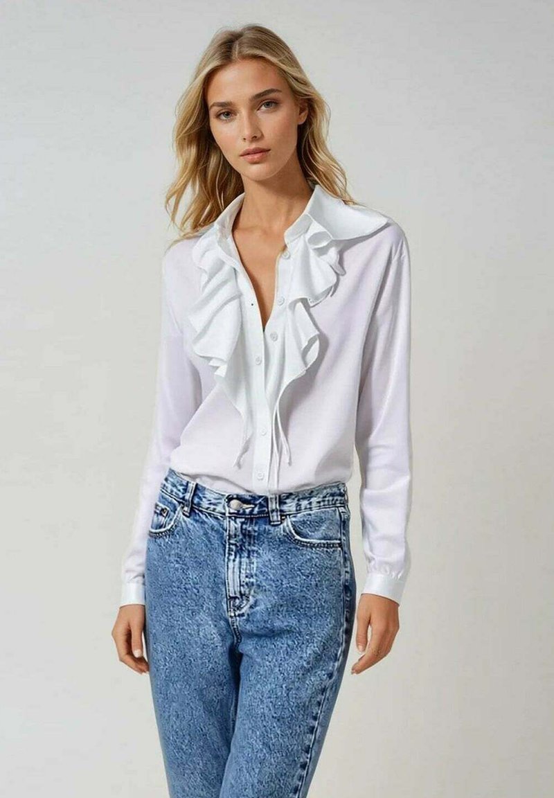 Blouse blanche à manches longues avec col à volants et devant à boutons, associée à un jeans taille haute bleu clair. Tissu lisse et coupe décontractée.