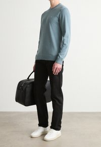 Jasnoniebieski sweter z długim rękawem, czarne spodnie i białe sneakersy, trzymający czarną skórzaną torbę. Prosty design, dopasowany kształt, gładka tekstura.