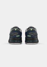 Par tenisica New Balance 1000 u tamnoplavoj i sivoj boji viđenih odostraga, prikazujući logotipe "1000" i "N" na svakom petnom dijelu.