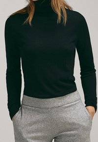 Maglione nero a collo alto con maniche lunghe, realizzato in un tessuto morbido; abbinato a pantaloni grigi chiari, in tessuto testurizzato, a vita alta.