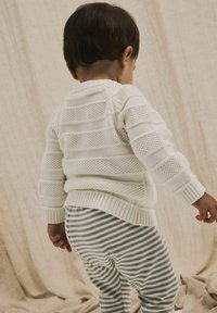 Maglione bianco lavorato a maglia con righe orizzontali testurizzate, abbinato a pantaloni a righe grigie e bianche. L'attenzione è sul retro e sul profilo.